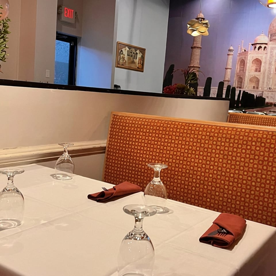 Elegant restaurant dining area with white tablecloths, red napkins, patterned booths, and a Taj Mahal mural.