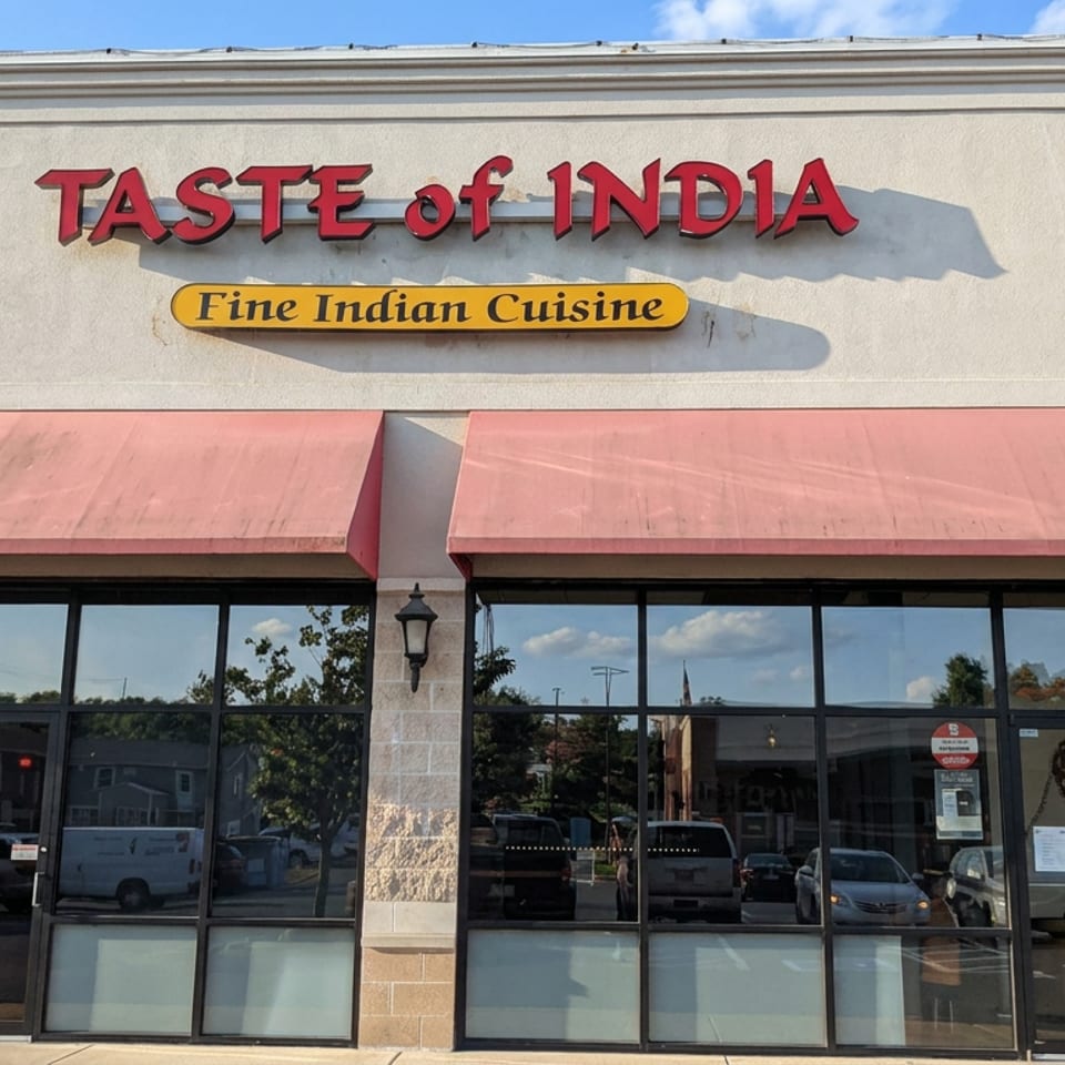 Exterior storefront of Taste of India Fine Indian Cuisine with red awnings, glass doors, and an illuminated open sign.